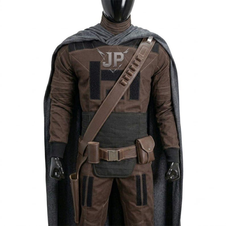 May include: A brown and black tactical costume set featuring a long grey cape, a brown long-sleeve shirt with black panels and the letters JP on the chest, a brown utility belt with a holster and pouch, and a diagonal shoulder strap with loops.