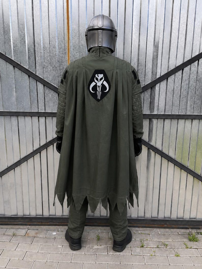 Puede incluir: Un disfraz de cuerpo completo que incluye un casco de color plata met&aacute;lica y una chaqueta verde oliva con mangas acolchadas. Una capa larga a juego de color verde oliva cuelga de los hombros, mostrando un emblema de cr&aacute;neo de Mythosaurio en la espalda.