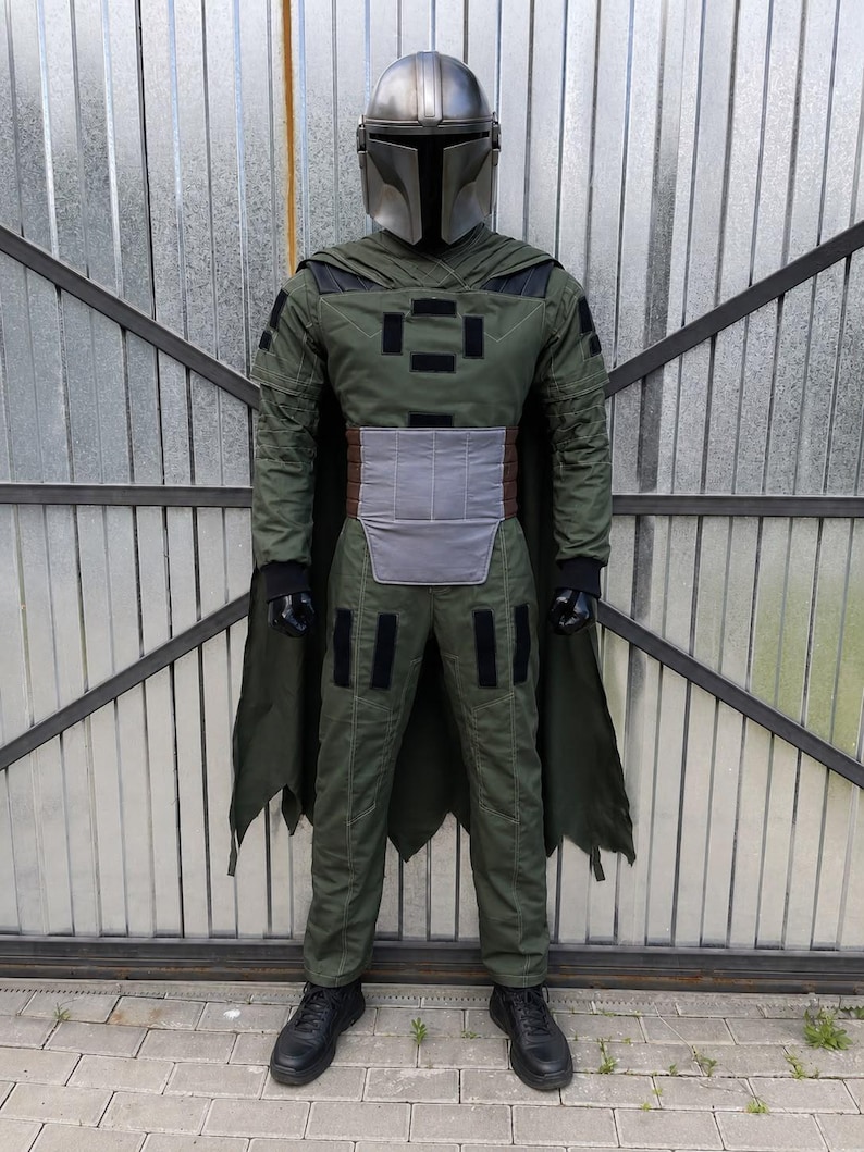 Puede incluir: Un disfraz de cuerpo completo que incluye un casco plateado met&aacute;lico con visera en forma de T, una chaqueta de manga larga verde oliva con pantalones a juego, una placa abdominal gris, guantes negros, zapatos negros y una capa verde oscuro.