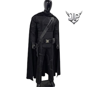 May include: A black tactical costume set featuring a long cape, a long-sleeved top with stitched paneling, matching trousers, and a utility belt with a holster and pouches. The ensemble includes a logo with the letters JP in the upper right corner.