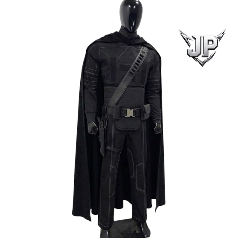 May include: A black tactical costume set featuring a long cape, a long-sleeved top with stitched paneling, matching trousers, and a utility belt with a holster and pouches. The ensemble includes a logo with the letters JP in the upper right corner.
