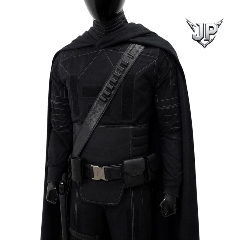 May include: A black costume set featuring a long cape, a long-sleeved shirt with subtle geometric stitching, and a utility belt with multiple pouches and a silver buckle. A diagonal shoulder strap with ammunition loops crosses the chest.