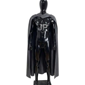 May include: A full-length grey cape draped over a glossy black mannequin. The cape features a prominent silver embroidered logo on the chest area displaying the letters JP with stylised wing-like accents extending from the top of the letters.