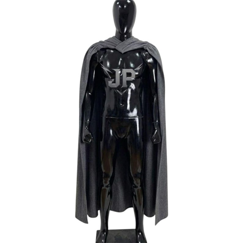 May include: A full-length grey cape draped over a glossy black mannequin. The cape features a prominent silver embroidered logo on the chest area displaying the letters JP with stylised wing-like accents extending from the top of the letters.