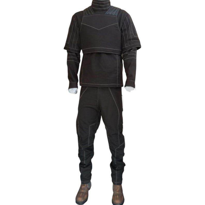 K&ouml;nnte beinhalten: Ein schwarzes Set aus lang&auml;rmeligem Oberteil und passender Hose mit hohem Kragen und strukturiertem Brustaufsatz. Das Kleidungsst&uuml;ck ist mit markanten wei&szlig;en Ziern&auml;hten an &Auml;rmeln, Rumpf und Beinen versehen und wird mit braunen Stiefeln kombiniert.