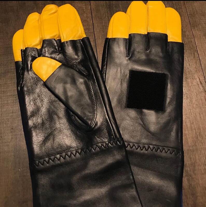 Puede incluir: Un par de guantes de cuero negro y amarillo con acabado liso. Los dedos son amarillos, mientras que las palmas y los pu&ntilde;os son negros. Los guantes incluyen un parche cuadrado negro de cierre de gancho y bucle en el dorso y costuras en zigzag.
