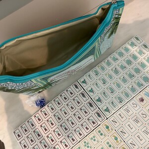 May include: A teal zipped pouch with a botanical print containing a set of mahjong tiles. The tiles feature various green and blue illustrations, Chinese characters, and the word NEWS. A small plastic bag with blue dice is included in the set.