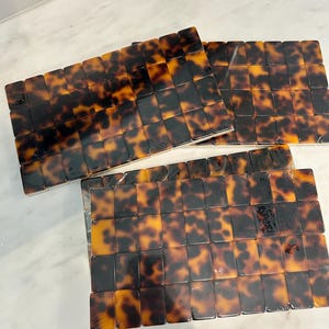 May include: A set of three rectangular trays featuring a glossy tortoiseshell pattern in shades of amber, brown, and black. Each tray is constructed from a grid of small, uniform rectangular tiles with a smooth, reflective finish.