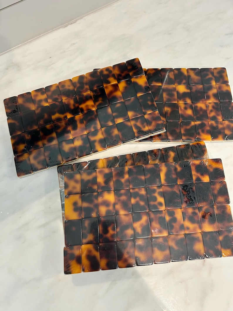 May include: A set of three rectangular trays featuring a glossy tortoiseshell pattern in shades of amber, brown, and black. Each tray is constructed from a grid of small, uniform rectangular tiles with a smooth, reflective finish.
