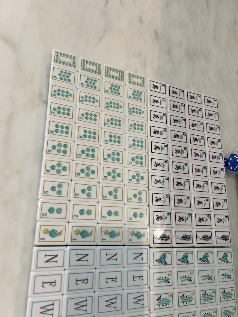 May include: A collection of white Mahjong tiles arranged in a grid. The tiles feature various green floral patterns, Chinese characters, and the word NEW printed in blue. Some tiles display numerical values, while others show intricate green designs.