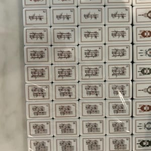 May include: A collection of rectangular Mahjong tiles arranged in a grid. The tiles feature white surfaces with brown and black illustrations of bamboo stalks, birds, and other symbols, along with small black numbers one through nine.