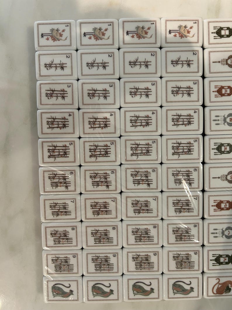 May include: A collection of rectangular Mahjong tiles arranged in a grid. The tiles feature white surfaces with brown and black illustrations of bamboo stalks, birds, and other symbols, along with small black numbers one through nine.
