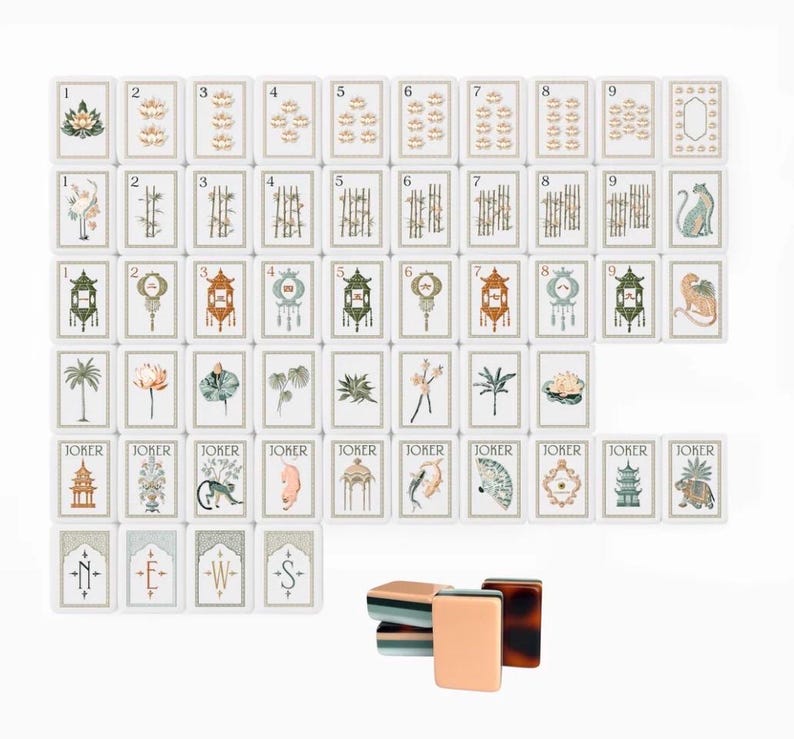 May include: A set of rectangular mahjong tiles featuring white faces with intricate illustrations of plants, animals, lanterns, and numbers. The tiles include Joker cards and directional markers labeled N, E, W, and S. A small stack of tiles is shown.