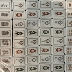 May include: A collection of white rectangular mahjong tiles arranged in a grid. The tiles feature black and red ink illustrations of bamboo stalks, numbered lanterns from one to nine, and stylized animal figures, all framed by thin borders.