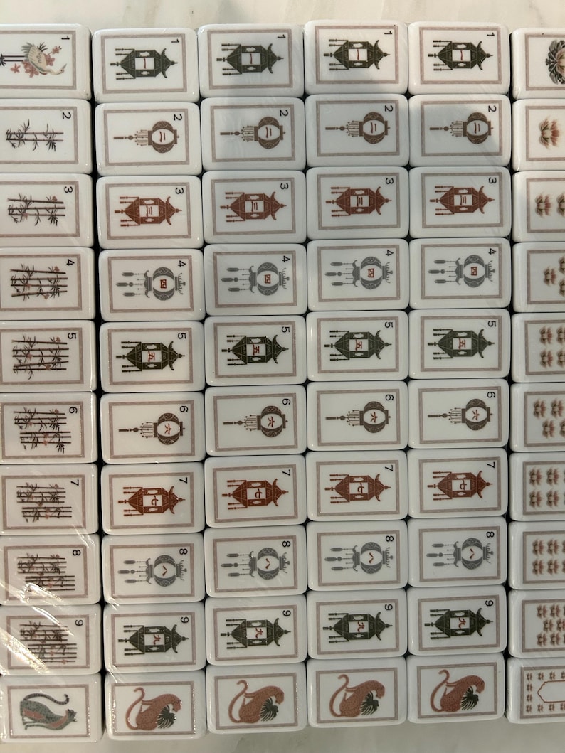 May include: A collection of white rectangular mahjong tiles arranged in a grid. The tiles feature black and red ink illustrations of bamboo stalks, numbered lanterns from one to nine, and stylized animal figures, all framed by thin borders.