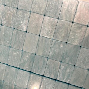 May include: A collection of rectangular tiles arranged in a grid pattern. Each tile features a light blue and white marbled finish with a glossy, pearlescent texture. The tiles are uniform in size and shape, creating a smooth, continuous surface.