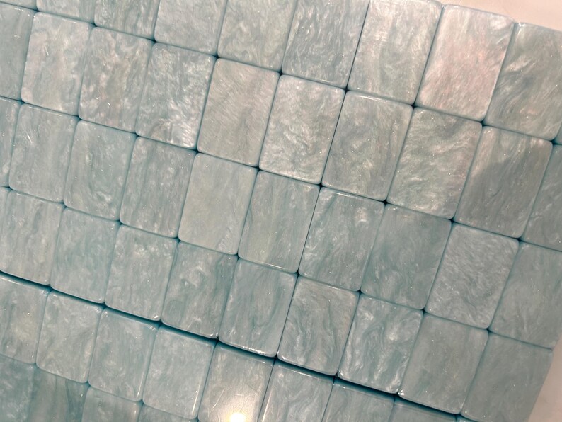 May include: A collection of rectangular tiles arranged in a grid pattern. Each tile features a light blue and white marbled finish with a glossy, pearlescent texture. The tiles are uniform in size and shape, creating a smooth, continuous surface.