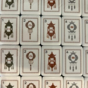 May include: A collection of rectangular white mahjong tiles arranged in a grid. Each tile features a thin border and a central illustration of a hanging lantern in green, brown, or gray. The tiles are numbered 1 through 4 in the top left corner.