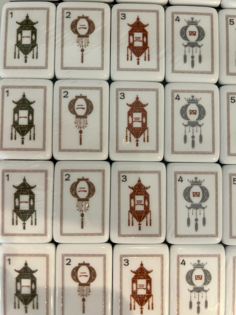 May include: A collection of rectangular white mahjong tiles arranged in a grid. Each tile features a thin border and a central illustration of a hanging lantern in green, brown, or gray. The tiles are numbered 1 through 4 in the top left corner.