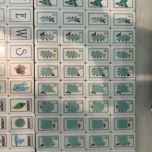 May include: A collection of white rectangular Mahjong tiles arranged in a grid. The tiles feature various illustrations including hummingbirds, bamboo stalks, sea life, and the word NEWS vertically. Each tile has a thin teal border and markings.