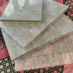 May include: A set of four rectangular mahjong tile racks stacked in a staggered formation. Each rack features a marbled light blue and white surface with a smooth, glossy finish, layered over a thin yellow and white base, all wrapped in clear plastic.
