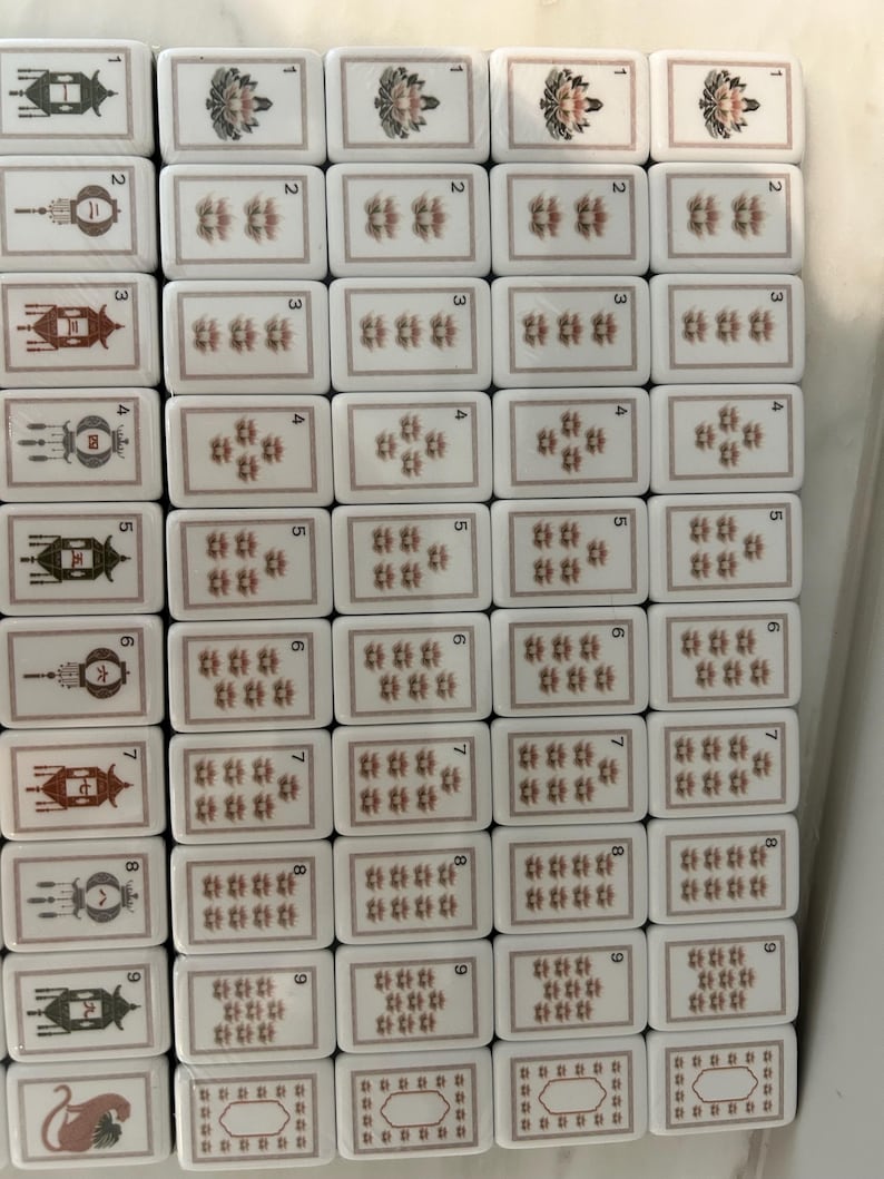 May include: A collection of rectangular mahjong tiles arranged in a grid. The left column features tiles with lantern illustrations and numbers one through nine, plus a cat tile. The remaining columns display tiles with floral patterns and numbers.