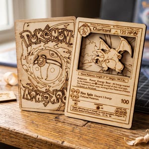 May include: Two laser-engraved wooden cards featuring Pokémon designs. One card displays the Pokémon logo and a Poké Ball, while the other depicts a Charizard character with text including 120 HP, Fire Spin, and various game statistics.