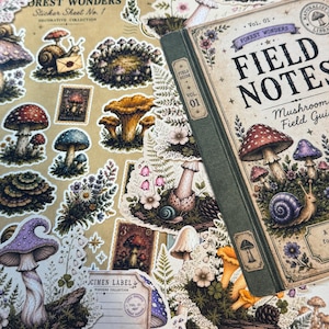 May include: A collection of decorative stickers featuring illustrations of mushrooms, snails, and wildflowers alongside a Field Notes Mushroom Field Guide book with a green spine and vintage-style botanical graphics and text.