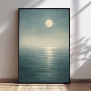 May include: A framed vertical wall art print depicting a full moon suspended in a hazy, pale blue sky above a calm, dark blue ocean. A bright, vertical reflection of the moonlight shimmers across the surface of the water in the center.