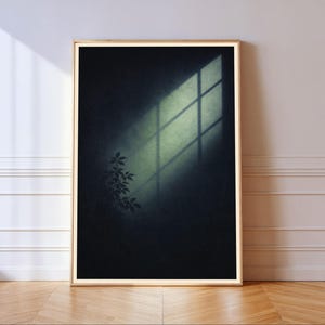 May include: A rectangular wall art print in a light wood frame featuring a dark, moody background with a bright, diagonal beam of light casting a window pane shadow and the silhouette of a small leafy plant in the lower left corner.