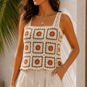 Op de afbeelding: Een mouwloze gehaakte top met een vierkante halslijn en een herhalend granny square-patroon in crème, olijfgroen en roestoranje, gecombineerd met een beige short met hoge taille, een knoopsluiting aan de voorzijde en zijzakken.