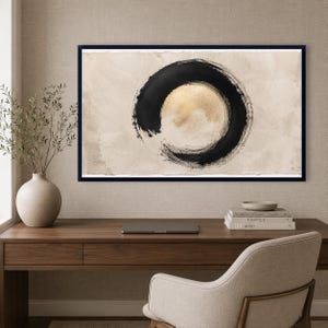 May include: A framed wall art print featuring a large, hand-painted black ink circle centered on a textured, light beige background. The interior of the circle reveals a soft, metallic gold wash, creating a contrast between the dark brushstrokes and the luminous center, all enclosed within a thin, dark frame.