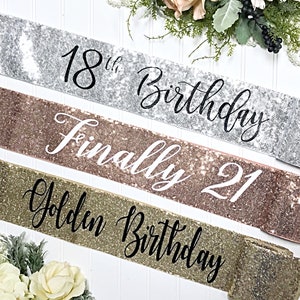 Op de afbeelding: Drie glitterende sjerpen voor een verjaardagsfeest. De sjerpen zijn zilver, rosé goud en goud. De zilveren sjerp zegt "18th Birthday". De rosé gouden sjerp zegt "Finally 21". De gouden sjerp zegt "Golden Birthday".