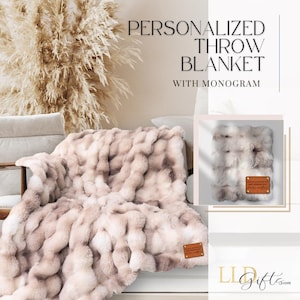 May include: A luxurious, personalised throw blanket with a monogram, in cream, brown, and grey tones. The blanket is draped over a white sofa. The image also includes the text "PERSONALIZED THROW BLANKET WITH MONOGRAM".