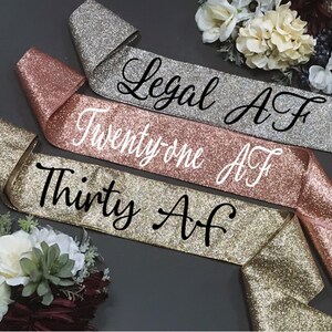 Puede incluir: Tres fajas de brillo dorado con texto negro. Las fajas dicen "Legal AF", "Twenty-one AF" y "Thirty AF".