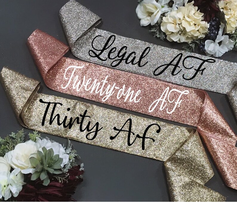 Puede incluir: Tres fajas de brillo dorado con texto negro. Las fajas dicen "Legal AF", "Twenty-one AF" y "Thirty AF".