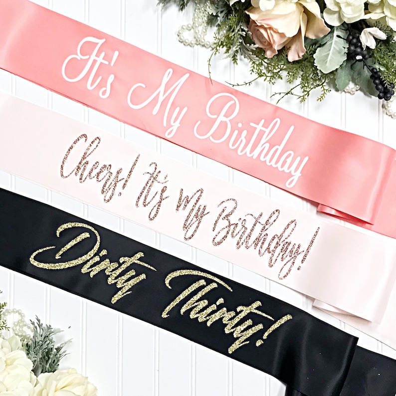 Puede incluir: Tres fajas de sat&eacute;n para una celebraci&oacute;n de cumplea&ntilde;os. La faja superior es rosa con texto blanco que dice "It's My Birthday". La faja del medio es blanca con texto de brillo dorado rosa que dice "Cheers! It's My Birthday!". La faja inferior es negra con texto de brillo dorado que dice "Dirty Thirty!"
