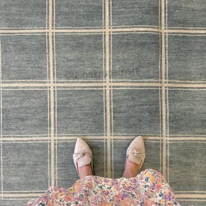 Peut inclure: Un grand tapis présentant un fond bleu ardoise avec un motif quadrillé composé de fines lignes beige clair. Le tapis possède une texture tissée et inclut le texte "ushakrugs.net" imprimé dans une police subtile et semi-transparente au centre.