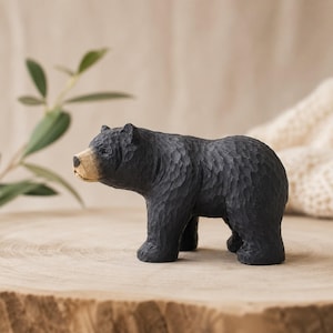 Könnte beinhalten: Eine handgeschnitzte Bärenfigur aus Holz mit einer strukturierten schwarzen Oberfläche am Körper und einem natürlichen hellbraunen Holzton an der Schnauze. Der Bär ist stehend dargestellt und weist sichtbare Meißelspuren auf.