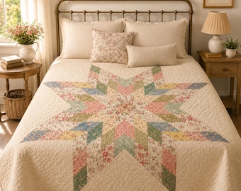 May include: A cream-colored quilt featuring a large central star pattern composed of various floral fabric patches in shades of pink, green, blue, and yellow. The quilt is displayed on a bed with matching floral and solid cream pillows.