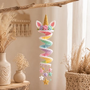 Può includere: Una decorazione a spirale a forma di unicorno realizzata all'uncinetto con un corno dorato, orecchie bianche con centri rosa e fiori pastello. Il corpo è una spirale multicolore gialla, verde, blu e rosa, rifinita con stelle all'uncinetto e perline dorate.