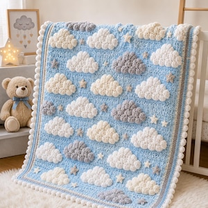 May include: A light blue crochet blanket featuring a repeating pattern of textured white and gray clouds interspersed with small stars. The blanket is finished with a white pom-pom border and a thin striped trim along the edges.