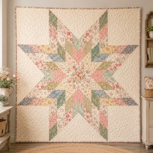 May include: A square quilt featuring a large central eight-pointed star pattern. The design is composed of various floral fabric patches in shades of pink, sage green, yellow, and blue, set against a cream-colored background with quilted texture.