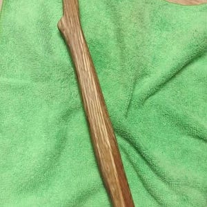 May include: A hand-carved wooden tool with a smooth, polished finish and a natural grain pattern. The object features a curved handle and a notched, fork-like head at the top end, showcasing the organic texture and light brown color of the wood.