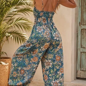 Puede incluir: Un mono de color verde azulado con un estampado floral vibrante en tonos naranja, blanco y verde. La prenda cuenta con tirantes finos, un cuerpo fruncido y perneras holgadas que se ajustan en los tobillos con puños elásticos.