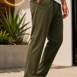 May include: Olive green trousers featuring a straight-leg cut, an elasticized waistband, and side pockets, paired with a plain white t-shirt and clean white sneakers. The garment displays a smooth, solid-colored fabric texture throughout.