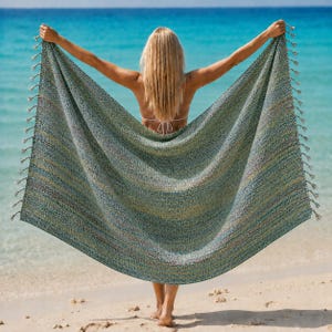 Könnte beinhalten: Ein rechteckiges, gewebtes Strandtuch mit einem variierenden Muster aus blaugrünen, grünen und gelben Fäden in strukturierter Optik. Das Tuch ist an beiden vertikalen Kanten mit langen, dünnen Fransen versehen, die einen dekorativen Rand bilden.