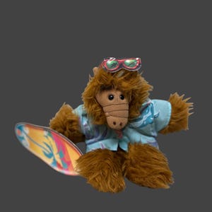 May include: A brown plush character with a long snout, wearing a light blue short-sleeved shirt with a white wave pattern. The character has red-rimmed sunglasses perched on its head and is holding a colorful surfboard with yellow, orange, and blue tones.