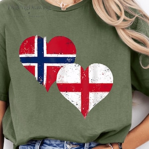 Può includere: Una t-shirt a maniche corte color verde oliva con due grafiche a forma di cuore sul davanti. Il cuore più grande mostra la bandiera norvegese, mentre il cuore più piccolo sottostante mostra la bandiera inglese. Entrambe hanno una texture usurata.