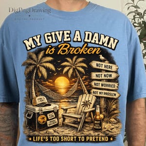 May include: A light blue t-shirt featuring a graphic of a beach scene at sunset with palm trees, a hammock, a wooden chair, a cooler, and a bottle. The text reads: MY GIVE A DAMN is Broken, NOT HERE, NOT NOW, NOT WORRIED, NOT MY PROSLEM, LIFE'S TOO SHORT TO PRETEND.